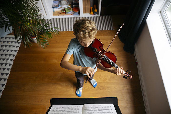 Boy with blond hair practicing violin in front of sheet music at home