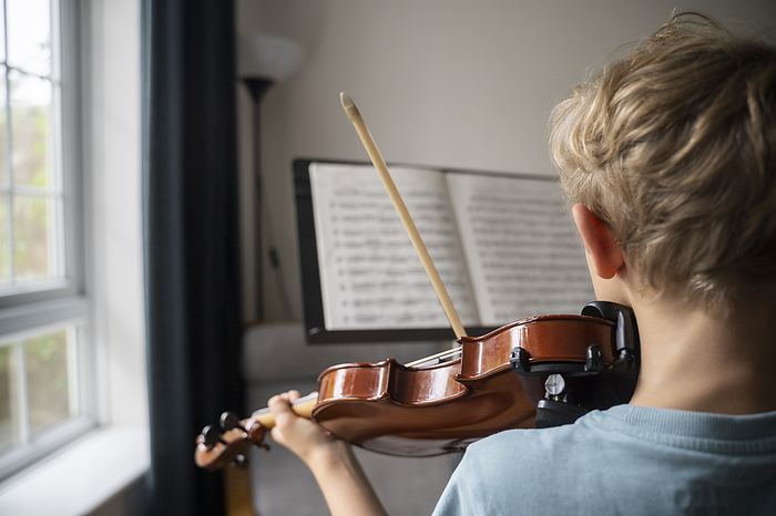 Boy practicing violin with sheet music at home
