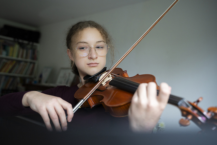 Girl wearing eyeglasses and playing violin at home