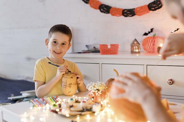 Smiling boy drawing on pumpkin with father at table