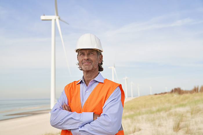 Thoughtful engineer wearing hardhat standing in front of wind turbines
