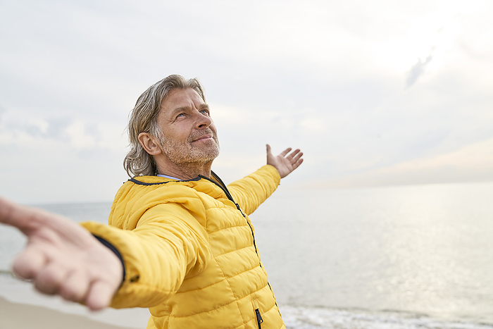 Smiling man with arms outstretched standing at beach
