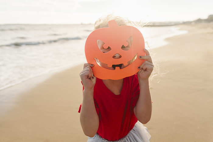 Girl covering face with Halloween mask at beach