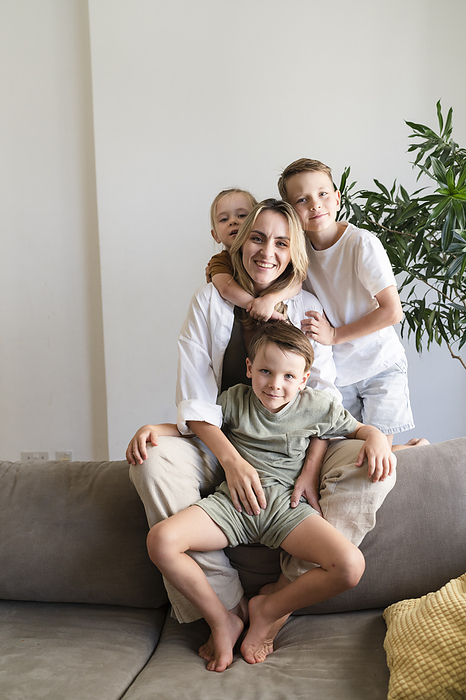 Smiling mother with three sons sitting on sofa at home