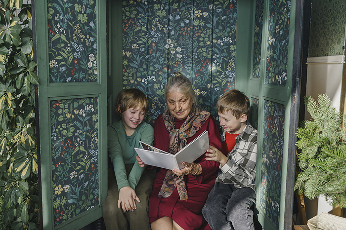 Great grandmother reading book to grandsons sitting in closet at home