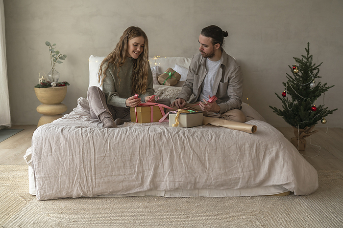 Smiling couple tying ribbons on Christmas presents at home