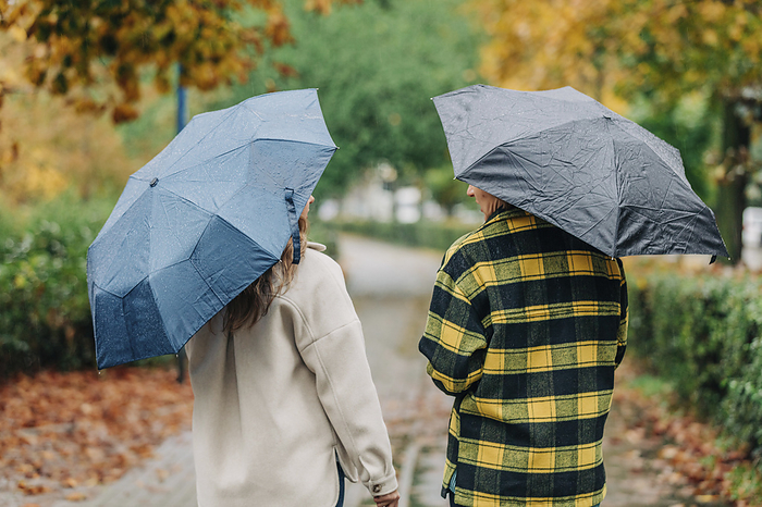 Mother and daughter holding umbrellas and walking in autumn park