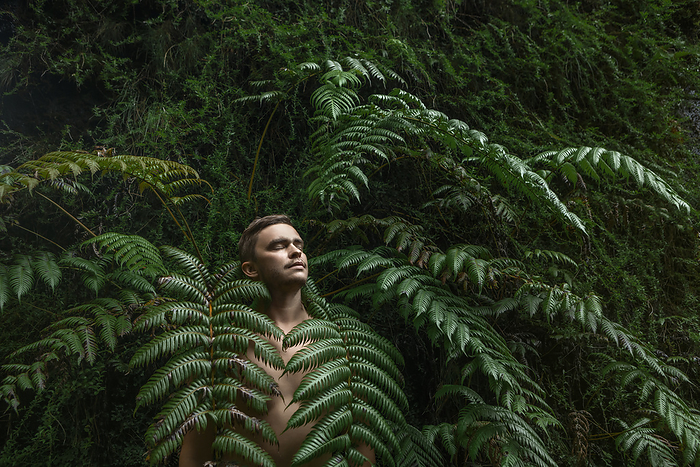 Shirtless man with eyes closed standing amidst fern plants