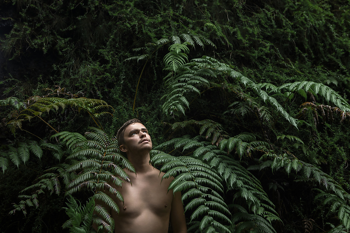 Shirtless man standing amidst fern plants