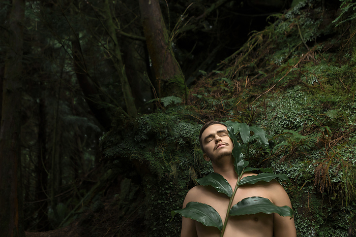 Young man standing with eyes closed and leaves in rainforest