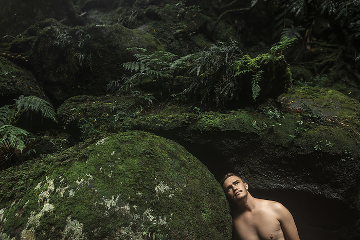 Thoughtful young man leaning on rock in rainforest