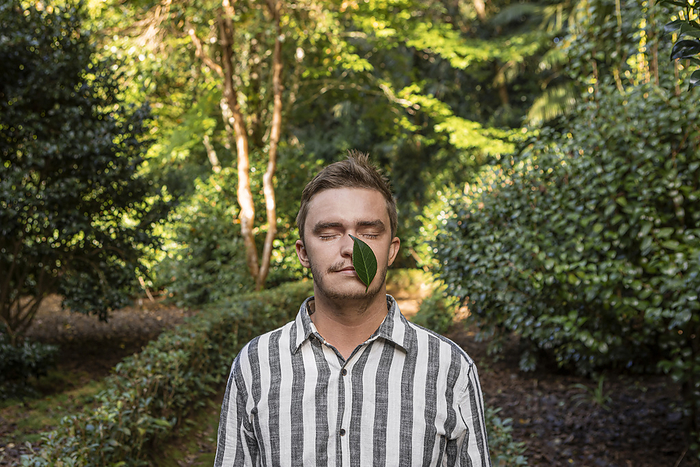 Young man with leaf over face in forest