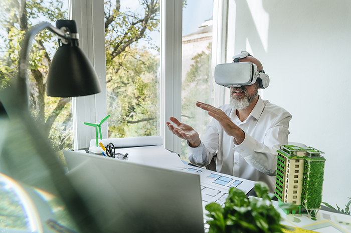 Architect wearing Virtual reality simulators gesturing at desk