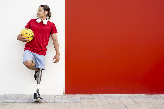 Man with disability holding yellow basketball and leaning on wall