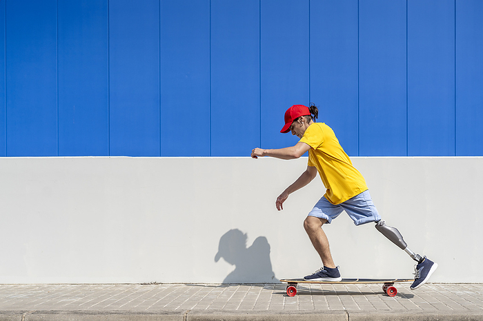Young man with disability skateboarding near wall