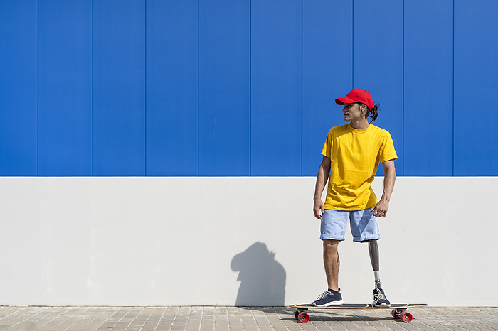 Young man with disability standing on skateboard near wall