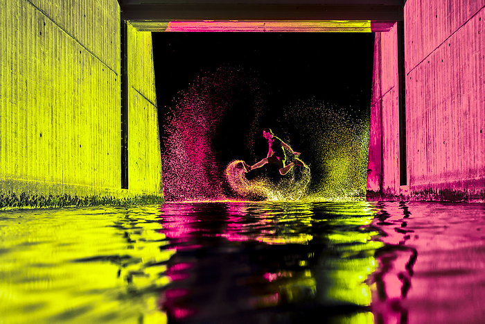 Young man jumping in river water with neon lights under bridge at night