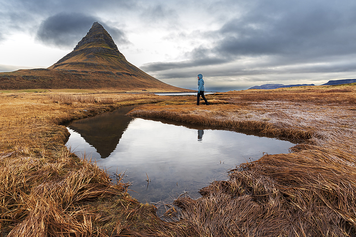 Woman walks in front of the famous Kirkjufell mountain reflecting in the water of a small lake, Snaefellsnes Peninsula, Western Iceland, Iceland Woman walks in front of the famous Kirkjufell mountain reflecting in the water of a small lake, Snaefellsnes Peninsula, Western Iceland, Iceland, Polar Regions, by Paolo Graziosi