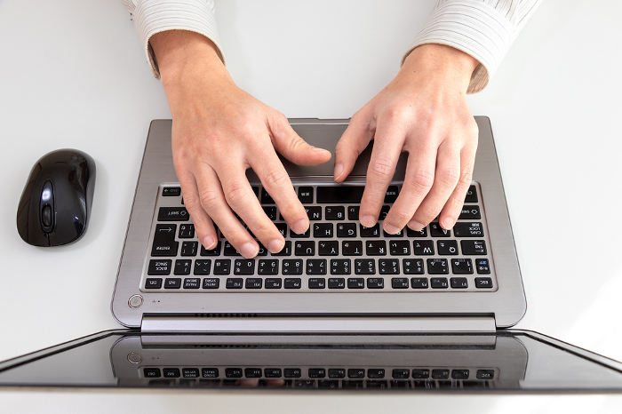 Top view of a person's hands typing on a laptop keyboard
