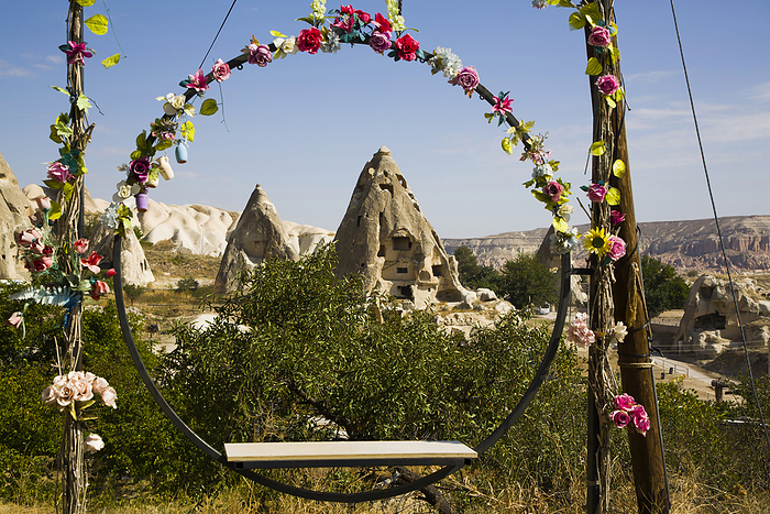 View through a circular swing seat decorated with silk flowers, of the Cave Houses carved into the rock formations against a blue sky near the town of Goreme in Pigeon Valley, Cappadocia Region; Nevsehir Province, Turkey, by Richard Maschmeyer / Design Pics