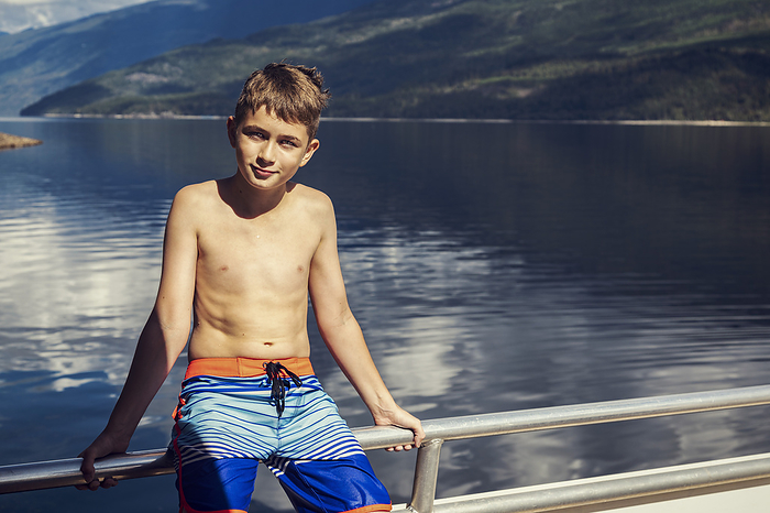 Portrait of a young boy sitting on the deck of a houseboat during a vacation while anchored along the shoreline of Shuswap Lake; British Columbia, Canada, by LJM Photo / Design Pics