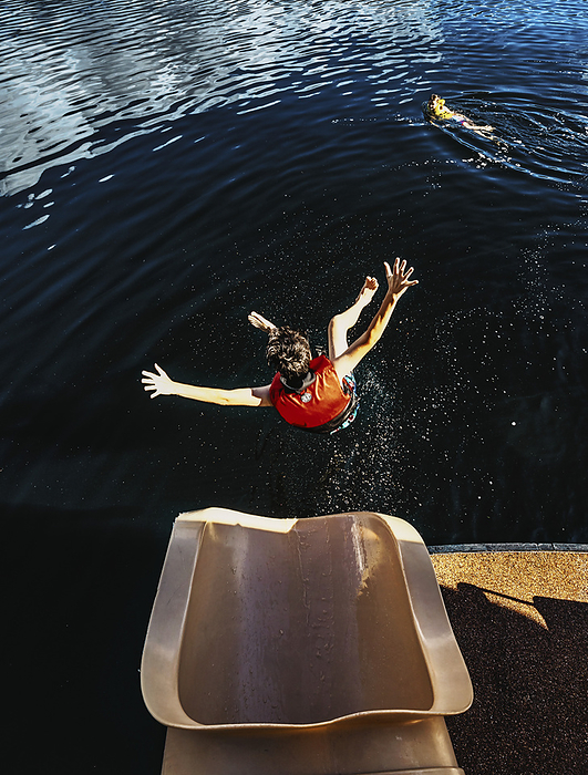 Boy flies mid-air towards the water after sliding out of the end of a houseboat waterslide on Shuswap Lake; British Columbia, Canada, by LJM Photo / Design Pics