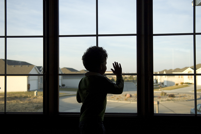 Toddler boy looks out the window of his home to the neighbourhood outside; Lincoln, Nebraska, United States of America, by Joel Sartore Photography / Design Pics