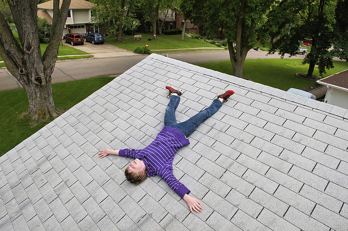 Elementary age boy laying on the shingled roof of a house; Elkhorn, Nebraska, United States of America, by Joel Sartore Photography / Design Pics