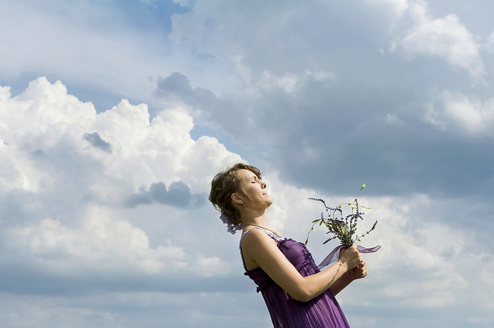 Woman holding flowers tightly in her hands against a cloud-filled sky; Firth, Nebraska, United States of America, by Joel Sartore Photography / Design Pics