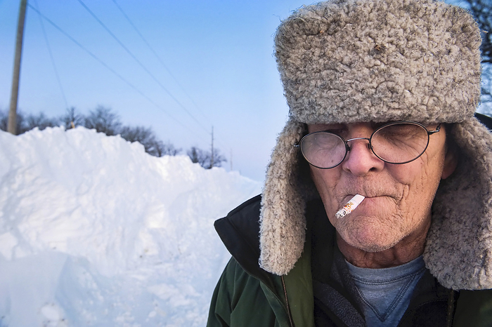 Man smoking a cigarette stands in the snow; Dunbar, Nebraska, United States of America, by Joel Sartore Photography / Design Pics