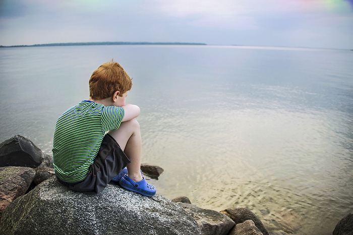 Young boy stares out over the water of Leech Lake in Minnesota, USA; Leech Lake, Minnesota, United States of America, by Joel Sartore Photography / Design Pics