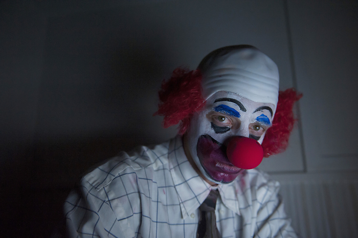 Close-up portrait of a clown sitting by himself in a dark room wearing a shirt and tie; Lincoln, Nebraska, United States of America, by Joel Sartore Photography / Design Pics