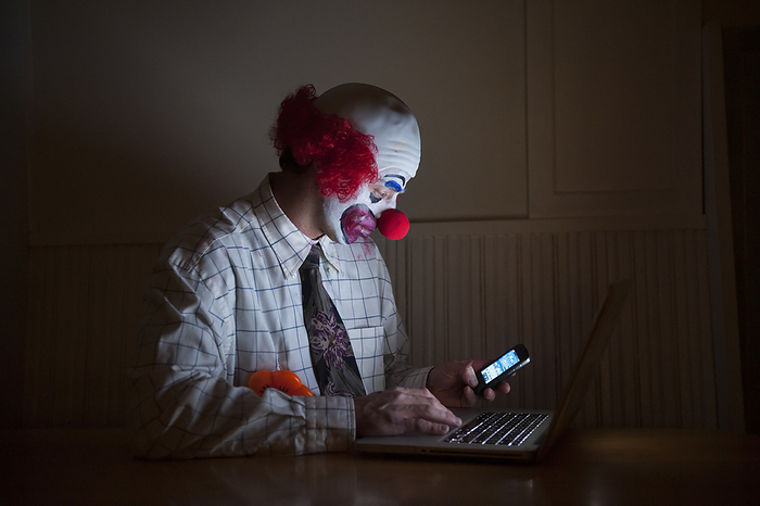 Clown wearing a shirt and tie uses a laptop computer and smart phone simultaneously; Lincoln, Nebraska, United States of America, by Joel Sartore Photography / Design Pics