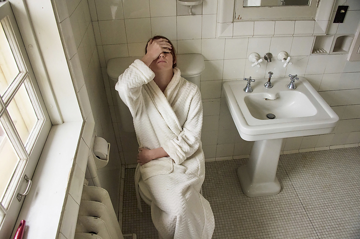 Young woman sits in a bathrobe holding her head in her bathroom; Lincoln, Nebraska, United States of America, by Joel Sartore Photography / Design Pics