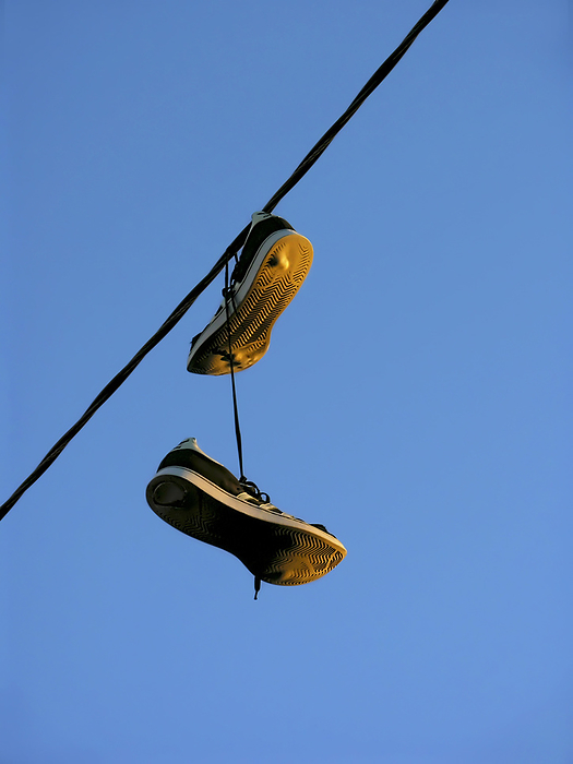 Shoes dangling from an overhead wire against a blue sky, by Amy D. White / Design Pics