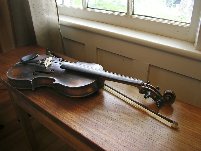 Antique fiddle and bow rest on a wooden bench lit by window light, by Amy D. White / Design Pics