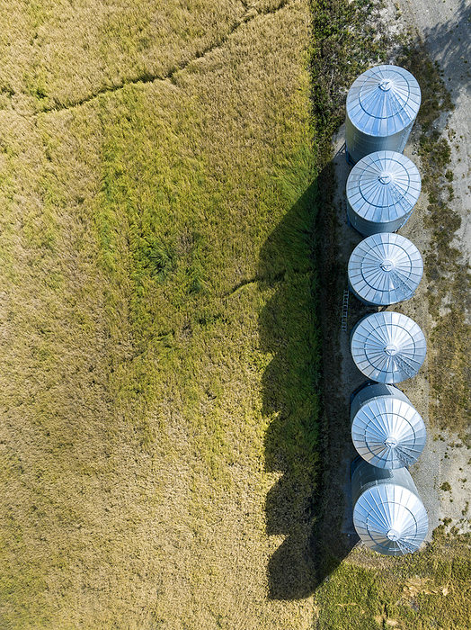 Aerial view of large metal grain bins in a row in a field, near Beiseker, Alberta; Alberta, Canada, by Michael Interisano / Design Pics