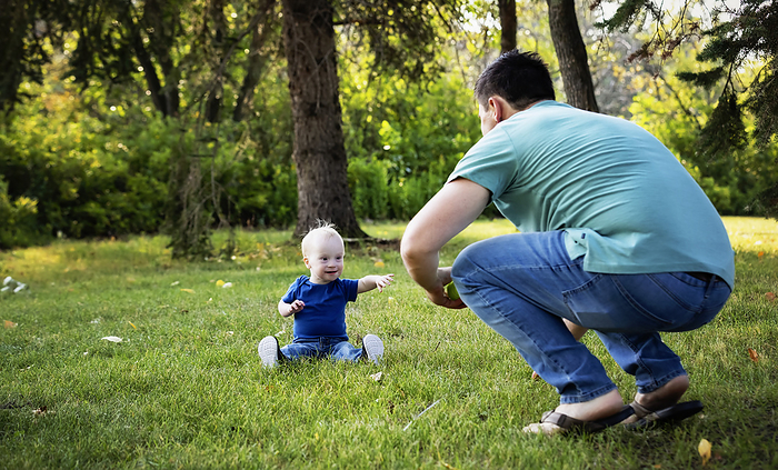 Father spending quality time and throwing a ball with his young son who has Down Syndrome, in a city park during a warm fall afternoon; Leduc, Alberta, Canada, by LJM Photo / Design Pics