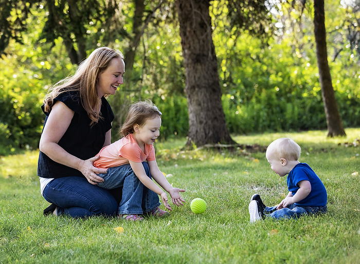 Mother throwing a ball with her daughter, and her young son who has Down Syndrome, in a city park during a warm fall afternoon; Leduc, Alberta, Canada, by LJM Photo / Design Pics