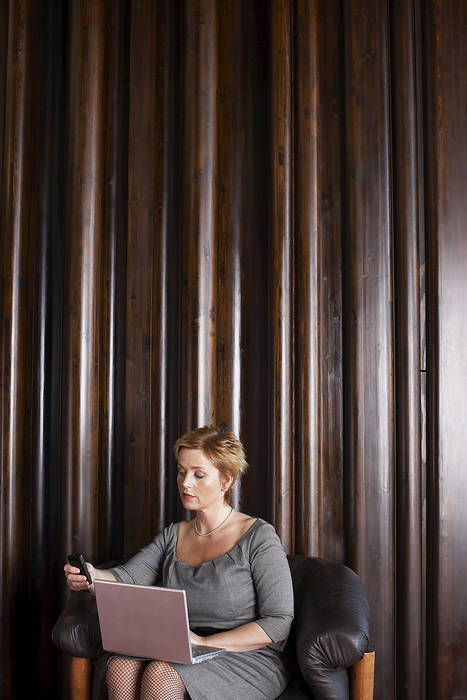 Woman in Foyer with Laptop Computer and Cellular Phone, by Masterfile / Design Pics