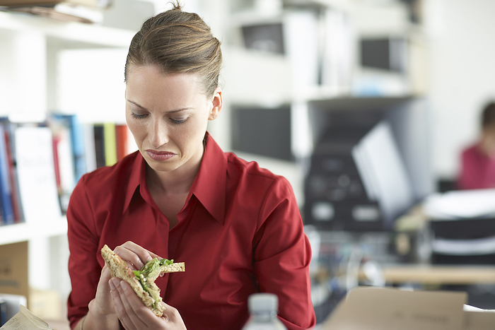 Businesswoman Looking at Sandwich, by Masterfile / Design Pics
