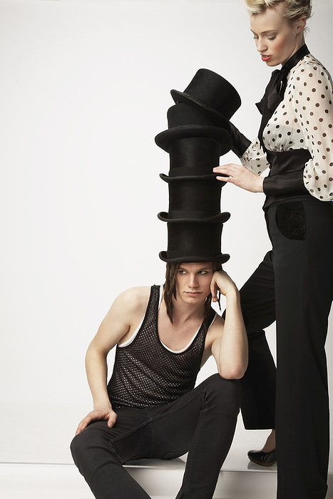 Woman Stacking Top Hats on Man, by Masterfile / Design Pics