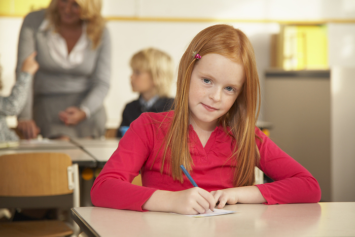 Portrait of Girl Sitting at Desk in Classroom, by Masterfile / Design Pics