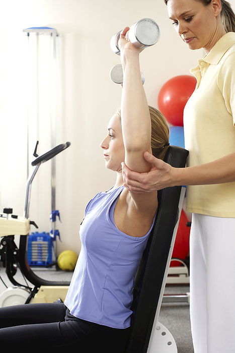 Physiotherapist Watching Woman using Free Weights, by Masterfile / Design Pics
