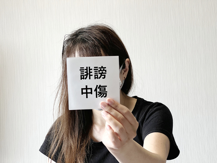 Woman holding a piece of paper with slanderous words in front of her face with one hand