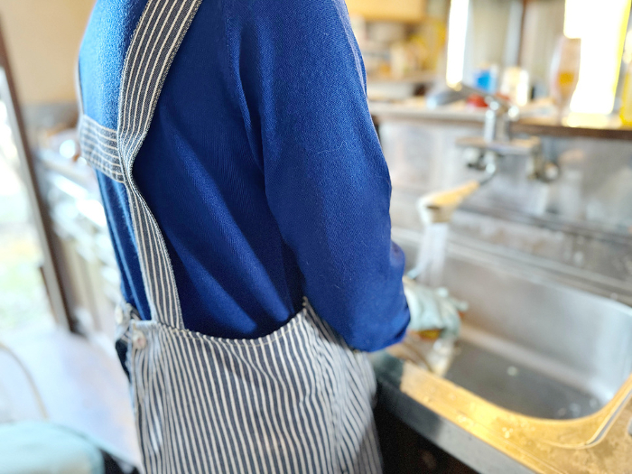 Woman in apron running water at kitchen sink