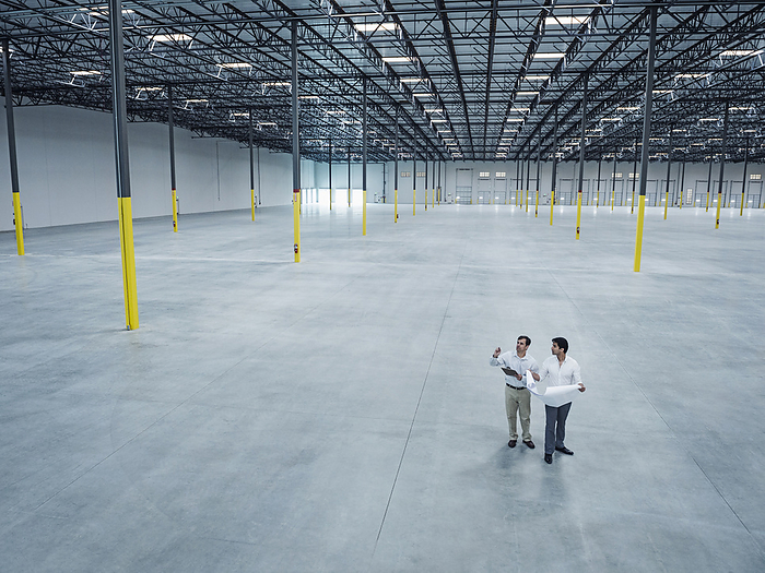 Architects with blueprint talking in empty warehouse, Fontana, California, USA, by Erik Isakson