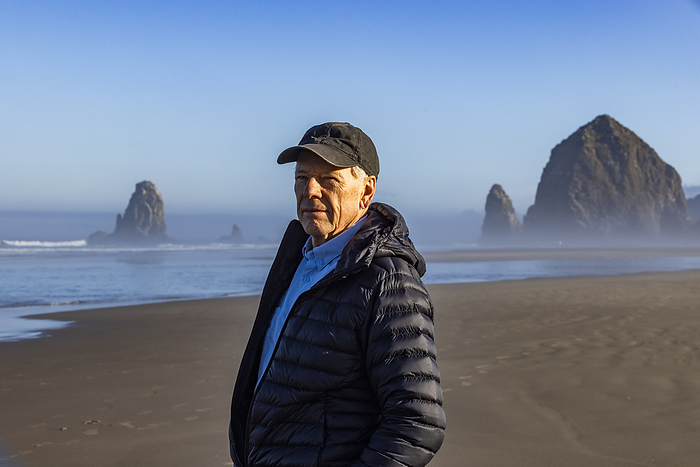 USA, Oregon, Portrait of man standing near Haystack Rock at Cannon Beach in morning mist, USA,Oregon,Cannon Beach, by Steve Smith