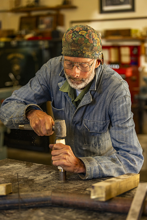 Senior artisan wood and metal craftsman works with tools in workshop, by Steve Smith