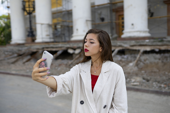 Portrait of young woman taking selfie with smart phone while standing in front of building, by Vyacheslav Chistyakov